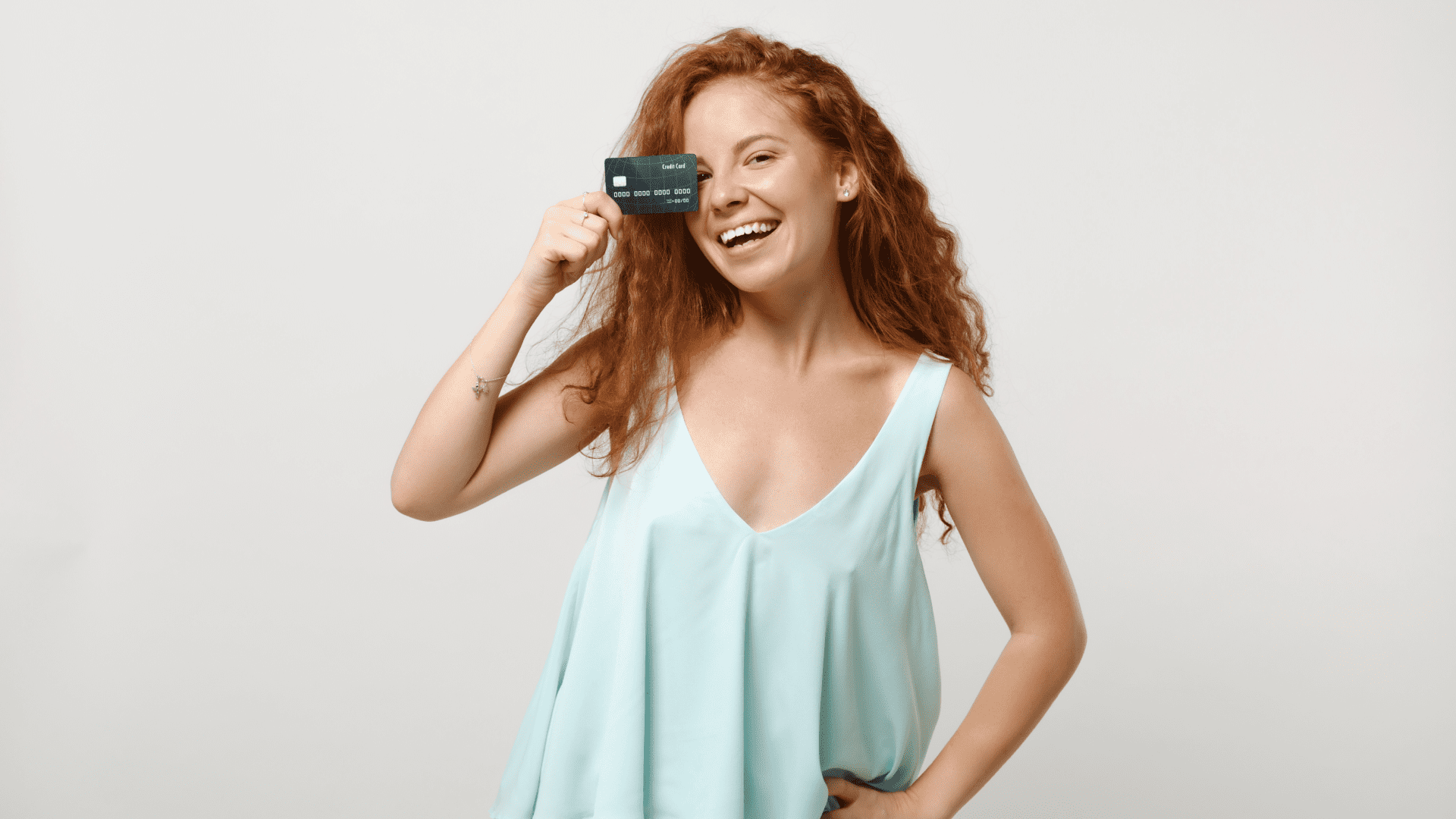Mujer joven pelirroja riendo y sosteniendo una tarjeta de crédito